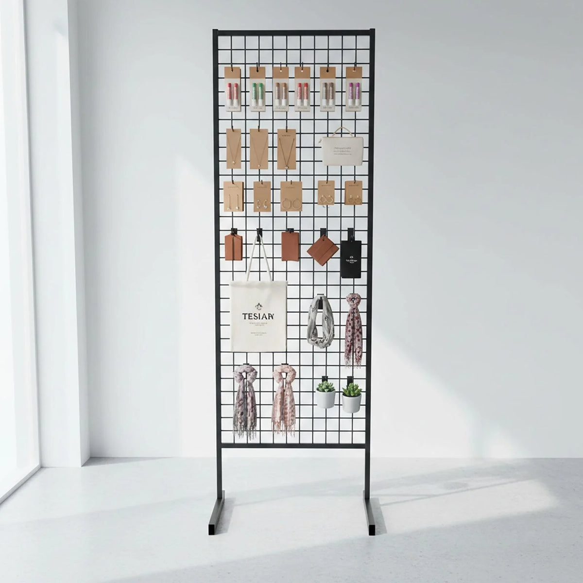 A black metal mesh display stand with hanging hooks, shown in a bright white room with various fashion accessories and a tote bag displayed on it.