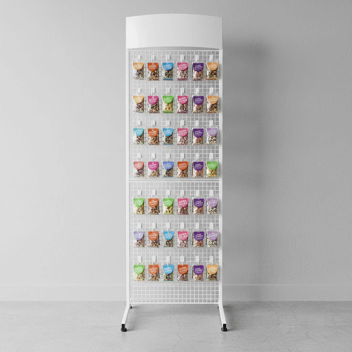 A white metal mesh display stand with multiple small  pouches hanging on its hooks, photographed against a plain light grey wall and floor.
